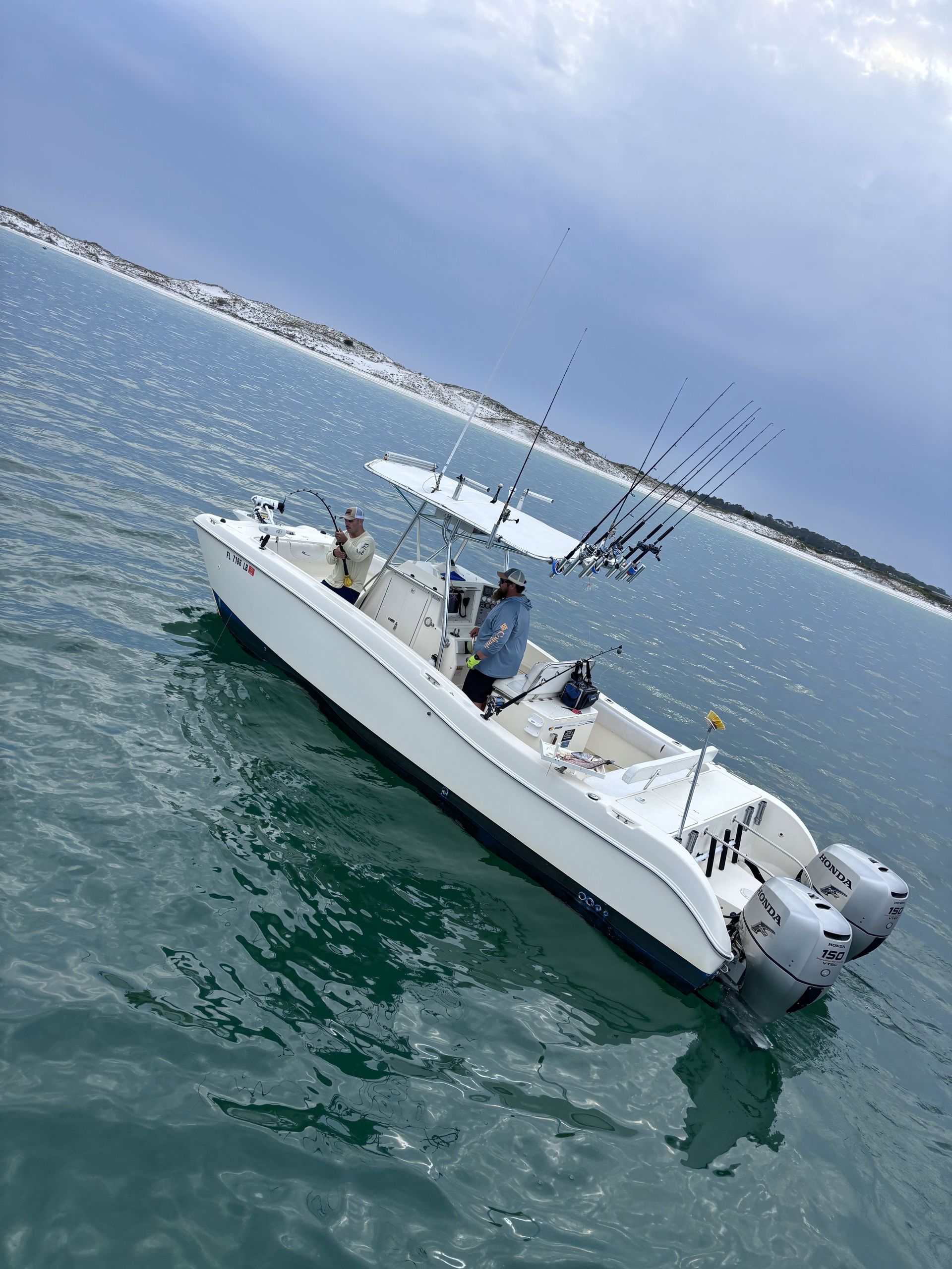White fishing boat on calm green water, with rods upright and people aboard under a cloudy sky.