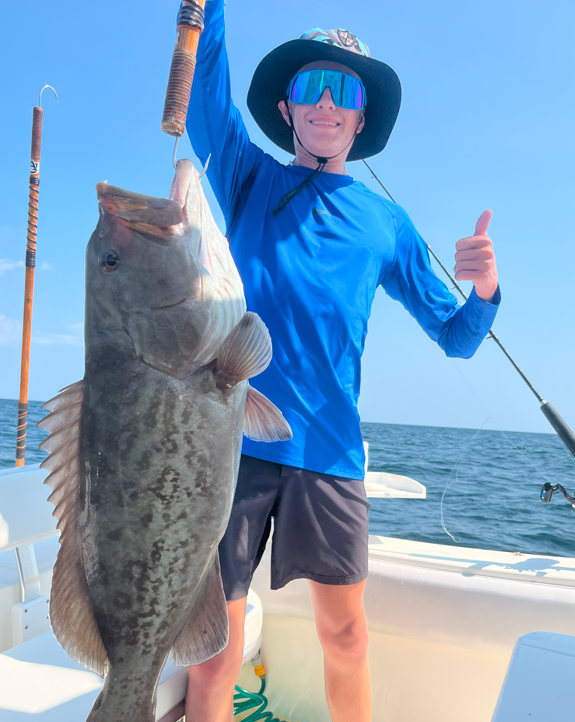 A man in a blue shirt is holding a large fish and giving a thumbs up